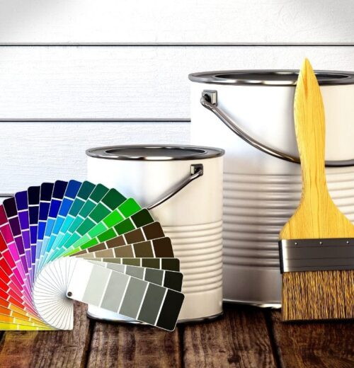 An array of color swatches fan out in front of three metal paint cans and a large paintbrush with a wooden handle.