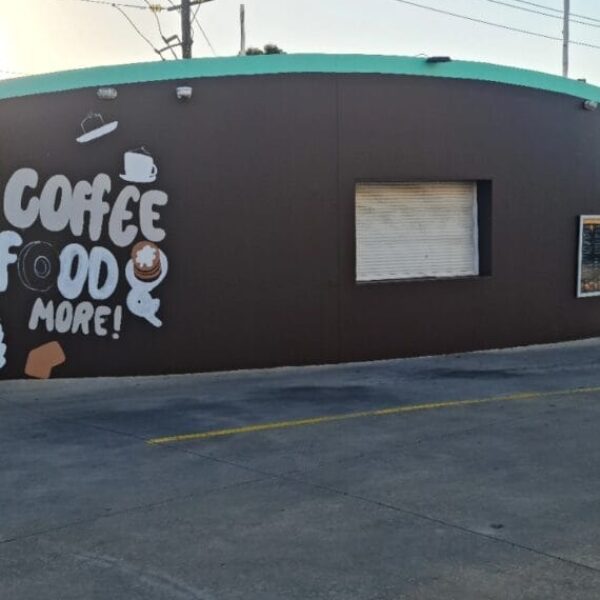 Exterior of a building with a brown wall, teal roof, and a mural on the left side featuring the text "COFFEE FOOD MORE!" along with illustrations of a coffee cup, donut, and plate of food.